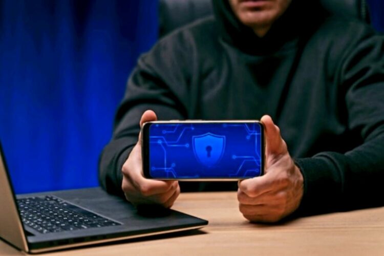 Hacker con sudadera negra y teléfono móvil en la mano