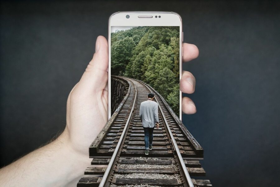 Un hombre camina por una vía de tren enmarcada dentro de un teléfono móvil que sostiene una mano.