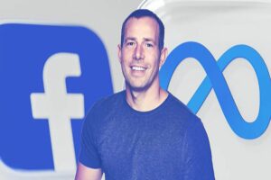 Un hombre con una camiseta azul cobalto sonríe delante de los logos de Facebook y Meta