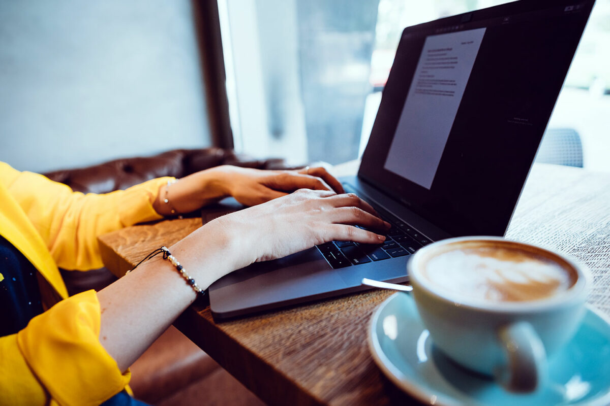Una mujer trabaja con un ordenador portátil junto a un café.